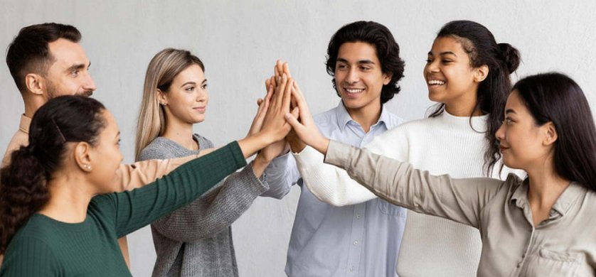 Un grupo de jóvenes profesionales diversos chocando las manos en el aire en señal de trabajo en equipo, cultura organizacional y compromiso laboral.