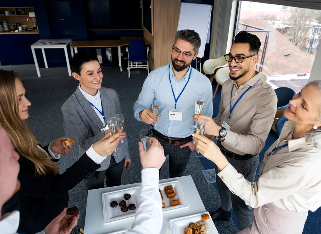 Eventos y activaciones internas Grupo de profesionales en traje brindando con copas durante un catering en la oficina.